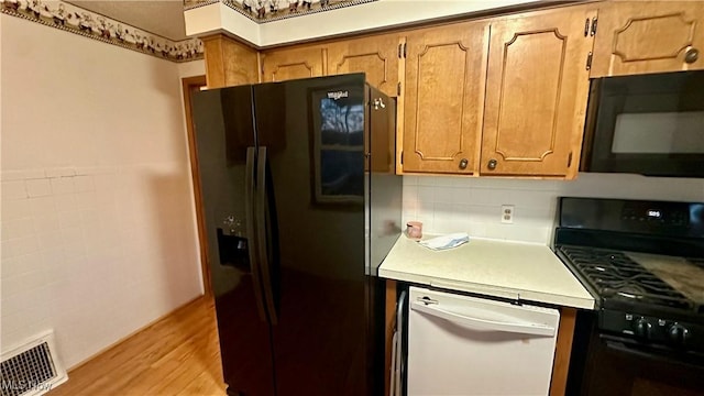 kitchen featuring decorative backsplash, light wood-type flooring, and black appliances