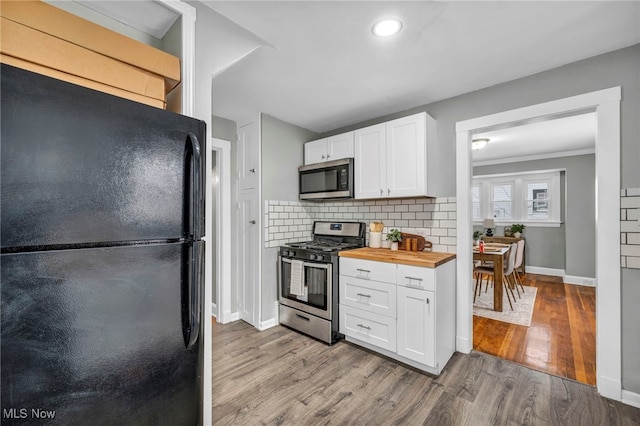 kitchen featuring butcher block counters, appliances with stainless steel finishes, tasteful backsplash, light hardwood / wood-style floors, and white cabinetry