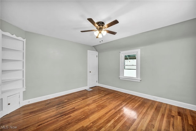 spare room with wood-type flooring, built in features, and ceiling fan