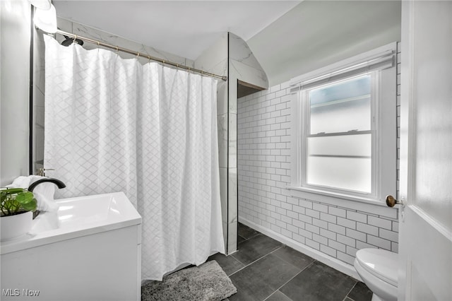 bathroom featuring walk in shower, vanity, vaulted ceiling, tile walls, and tile patterned flooring