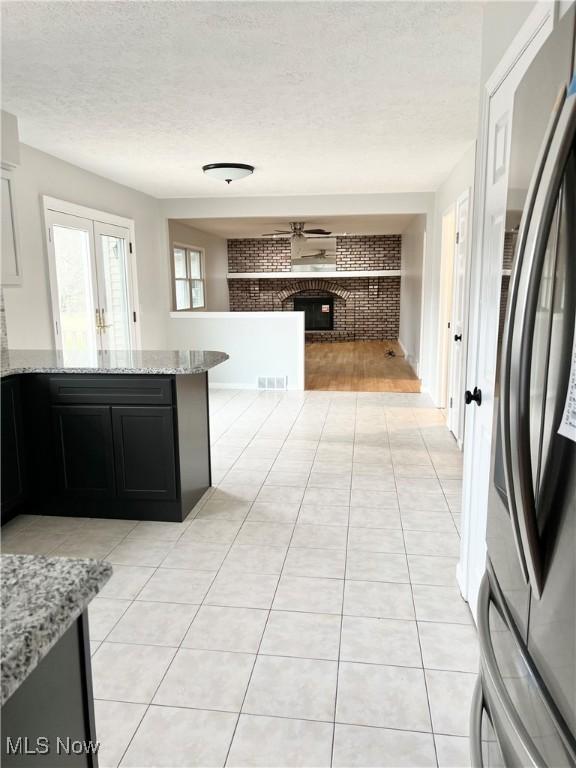 kitchen featuring light stone countertops, stainless steel fridge with ice dispenser, brick wall, and a brick fireplace