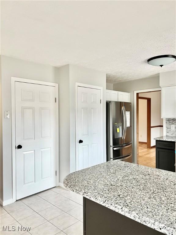 kitchen featuring white cabinets, light stone counters, and stainless steel refrigerator with ice dispenser