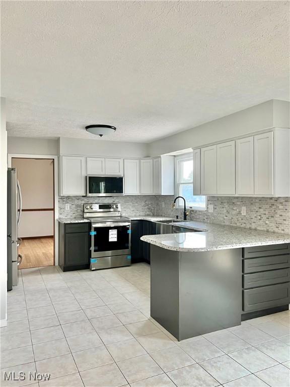 kitchen featuring white cabinetry, sink, kitchen peninsula, light tile patterned floors, and appliances with stainless steel finishes