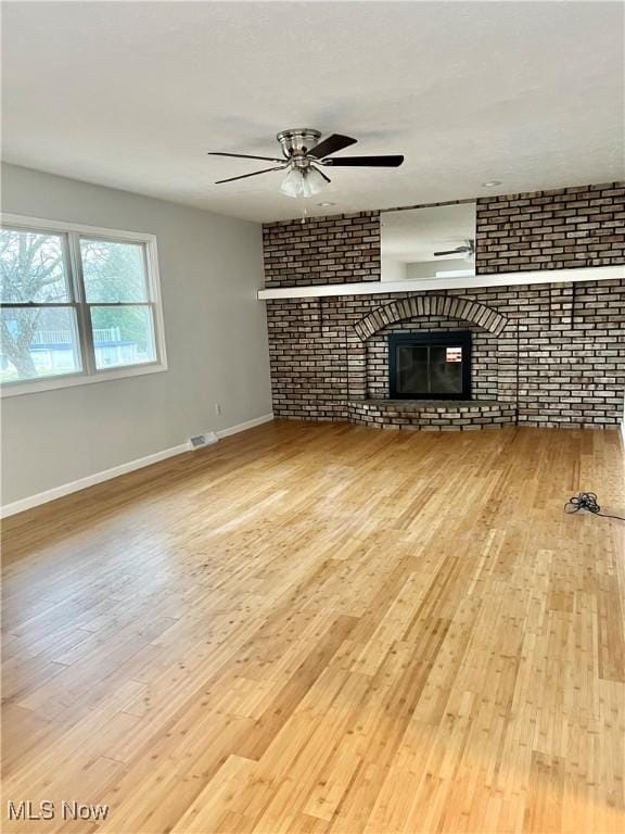 unfurnished living room with ceiling fan, light hardwood / wood-style floors, brick wall, and a brick fireplace