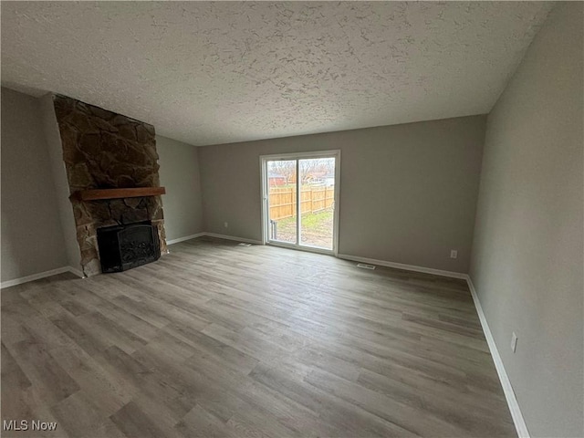 unfurnished living room with a textured ceiling, light wood-type flooring, and a stone fireplace