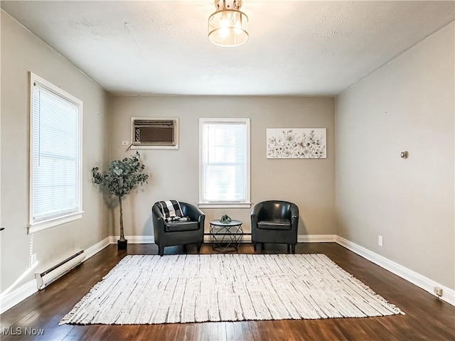 living area featuring a textured ceiling, dark hardwood / wood-style flooring, an AC wall unit, and a baseboard heating unit