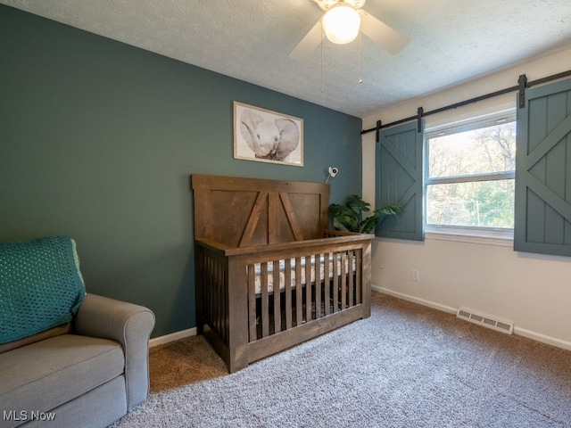 bedroom with carpet, ceiling fan, a barn door, and a textured ceiling