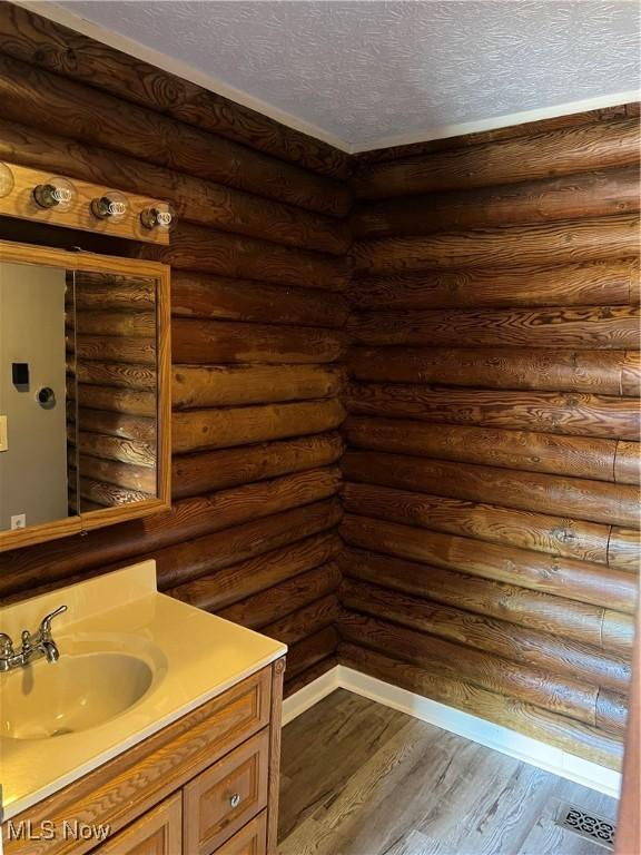 bathroom with log walls, hardwood / wood-style floors, a textured ceiling, and vanity