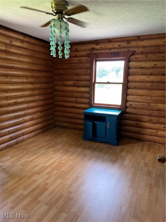 unfurnished room featuring hardwood / wood-style flooring, a textured ceiling, and log walls