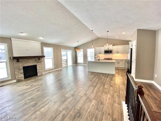 unfurnished living room featuring hardwood / wood-style flooring, vaulted ceiling, a stone fireplace, and sink