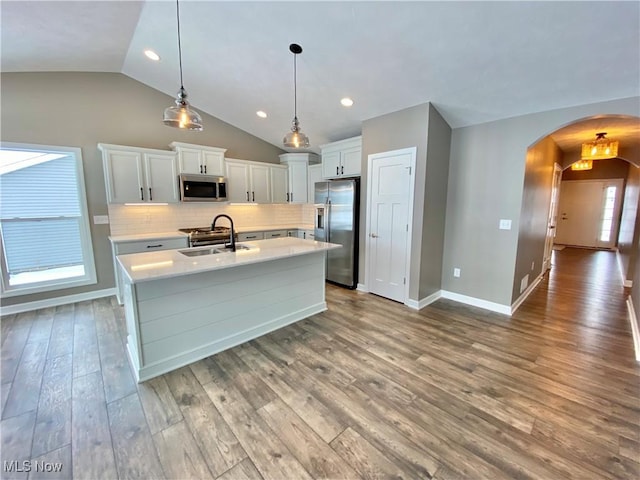 kitchen with sink, stainless steel appliances, pendant lighting, vaulted ceiling, and light hardwood / wood-style floors