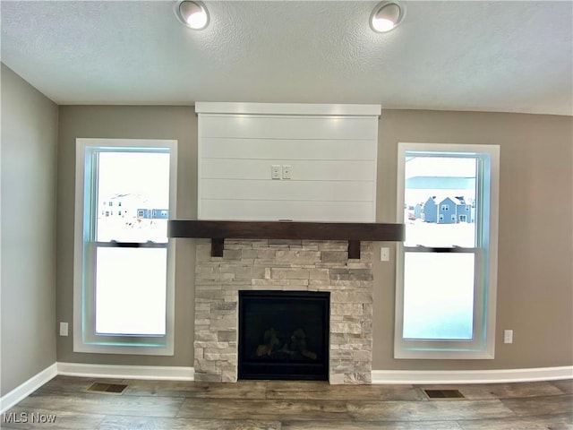 unfurnished living room with hardwood / wood-style floors, a fireplace, a wealth of natural light, and a textured ceiling