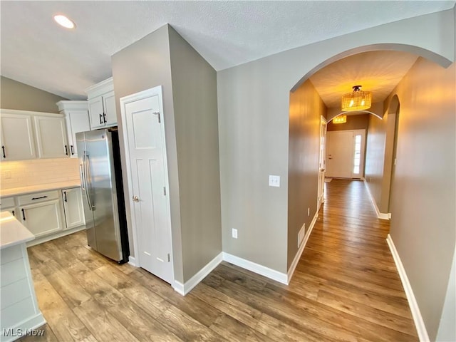 kitchen with light wood-type flooring, backsplash, vaulted ceiling, white cabinetry, and stainless steel refrigerator