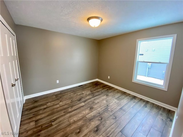 spare room with a textured ceiling and dark hardwood / wood-style floors