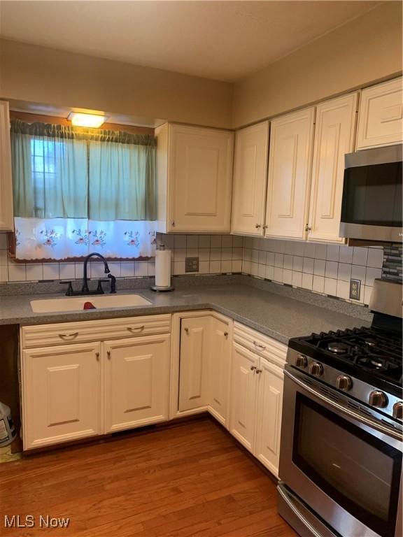 kitchen featuring white cabinets, sink, dark hardwood / wood-style floors, decorative backsplash, and appliances with stainless steel finishes