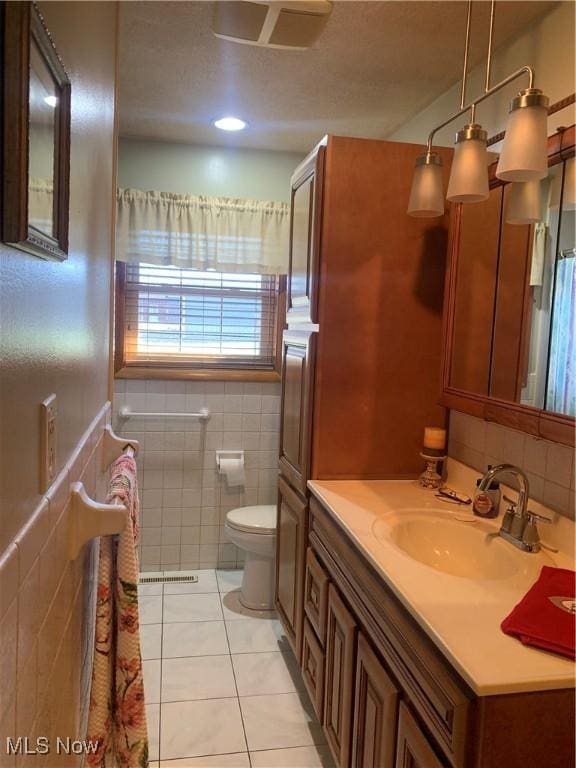 bathroom with toilet, vanity, tile patterned floors, and tile walls