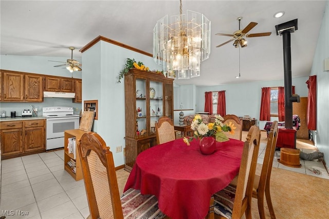 tiled dining room featuring ceiling fan with notable chandelier, vaulted ceiling, and a wood stove