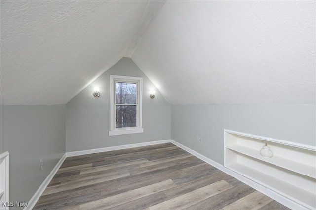 additional living space with built in shelves, wood-type flooring, a textured ceiling, and vaulted ceiling