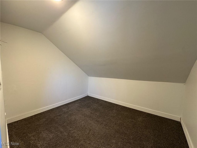 additional living space with vaulted ceiling and dark colored carpet