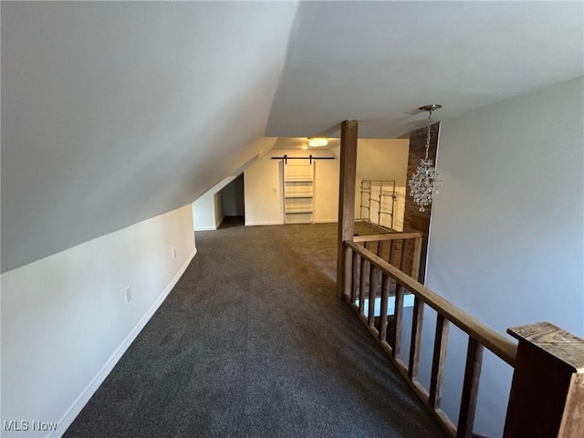 additional living space featuring vaulted ceiling, a barn door, and dark colored carpet