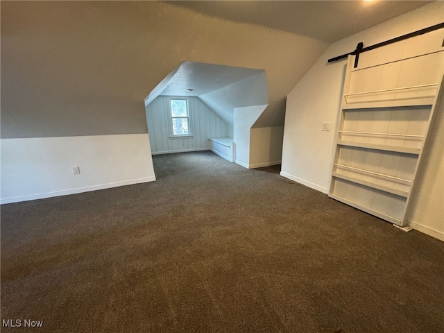 bonus room with a barn door, vaulted ceiling, and dark colored carpet