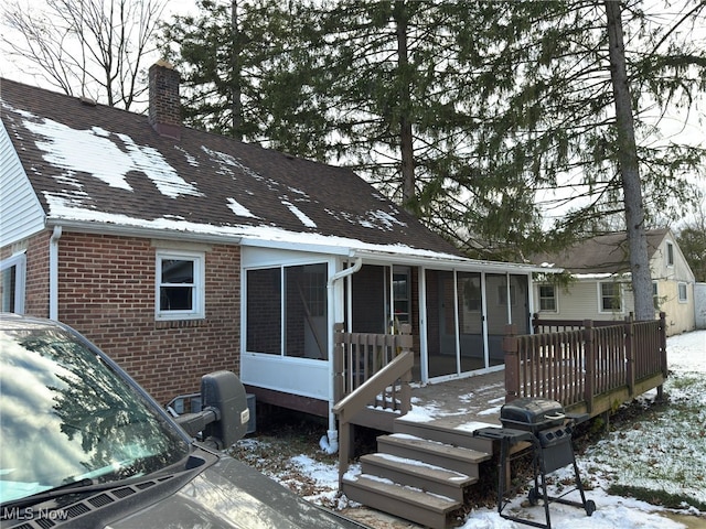 snow covered house with a wooden deck and a sunroom