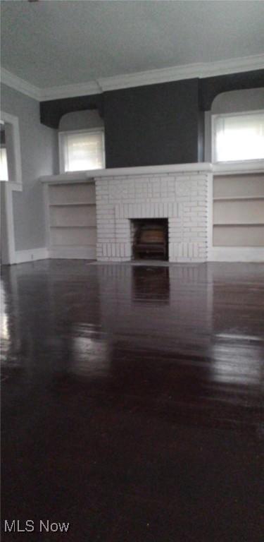 interior space with built in shelves, a wealth of natural light, a brick fireplace, crown molding, and wood-type flooring