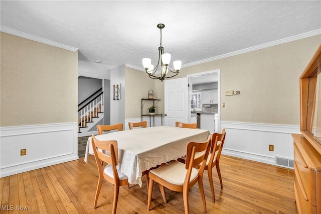 dining space with a textured ceiling, light hardwood / wood-style floors, crown molding, and a chandelier