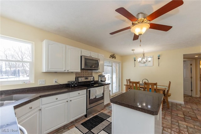 kitchen with a center island, white cabinets, stainless steel appliances, and ceiling fan with notable chandelier