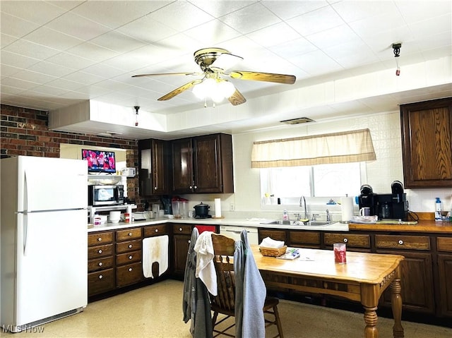 kitchen featuring white refrigerator, brick wall, sink, and dark brown cabinets