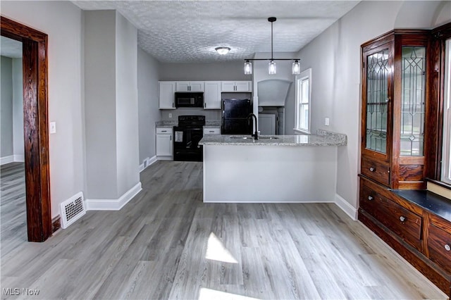 kitchen featuring pendant lighting, light wood-type flooring, white cabinetry, and black appliances