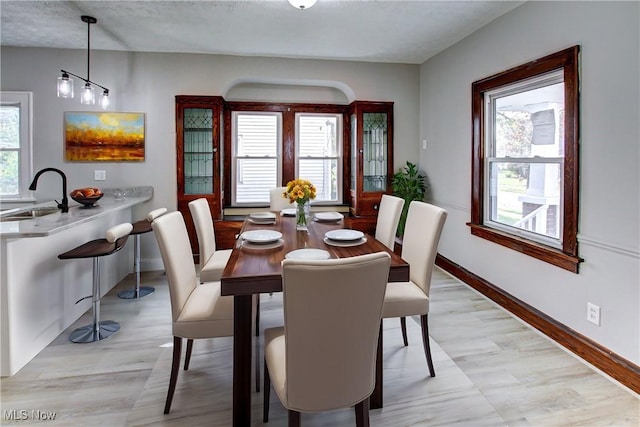 dining room with light wood-type flooring, a textured ceiling, a healthy amount of sunlight, and sink