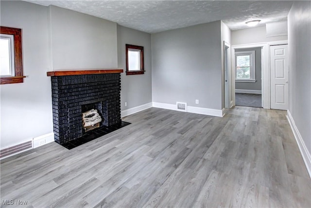 unfurnished living room with light wood-type flooring, a textured ceiling, and a brick fireplace