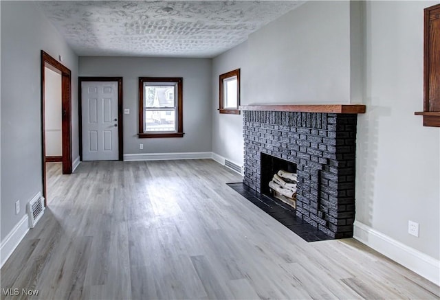 unfurnished living room with a fireplace, a textured ceiling, and light wood-type flooring