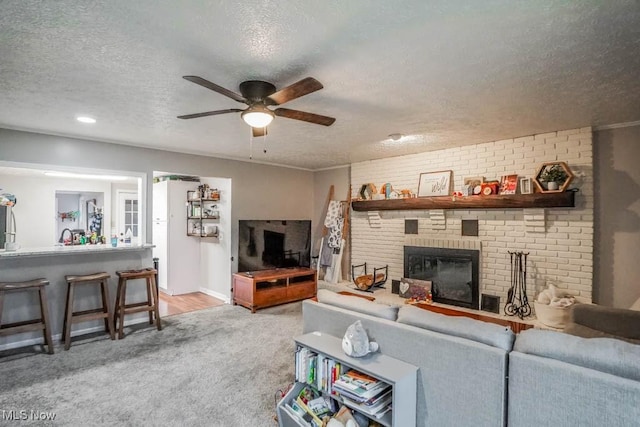 living room featuring ceiling fan, light colored carpet, a textured ceiling, and a brick fireplace