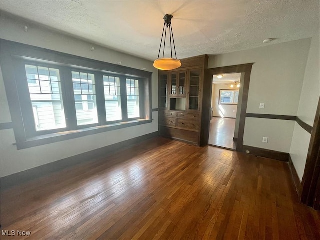 unfurnished dining area featuring a textured ceiling, dark hardwood / wood-style flooring, and plenty of natural light