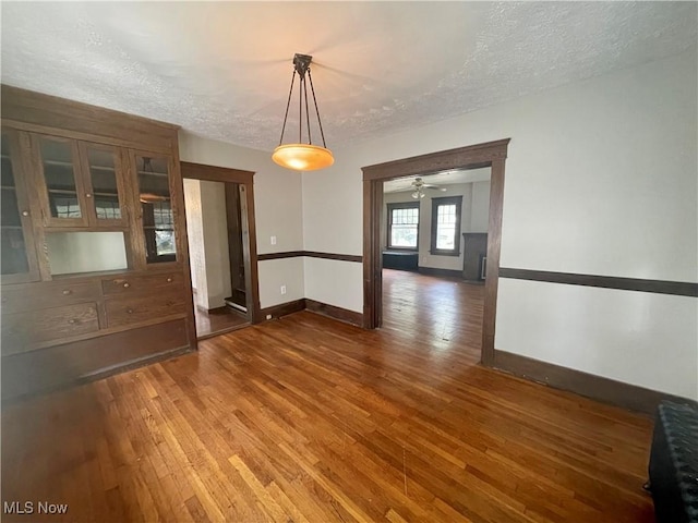 unfurnished dining area with a textured ceiling, ceiling fan, and dark wood-type flooring