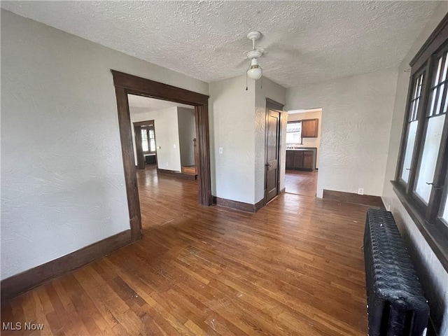 unfurnished living room featuring a textured ceiling, radiator heating unit, a healthy amount of sunlight, and dark hardwood / wood-style floors