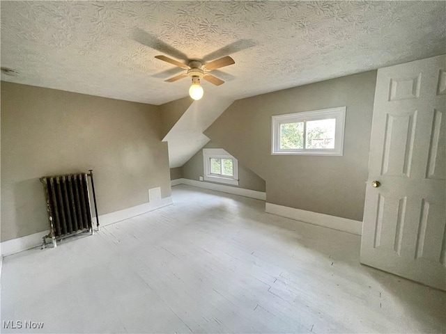 bonus room with ceiling fan, radiator heating unit, light hardwood / wood-style flooring, a textured ceiling, and lofted ceiling