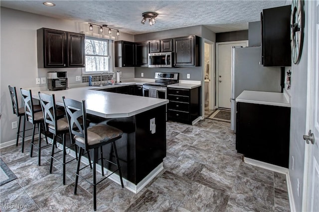 kitchen with sink, a kitchen breakfast bar, kitchen peninsula, a textured ceiling, and appliances with stainless steel finishes