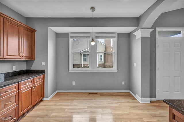 interior space with pendant lighting, light hardwood / wood-style floors, decorative columns, and dark stone counters