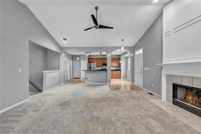 unfurnished living room with light carpet, high vaulted ceiling, ceiling fan, and a tiled fireplace