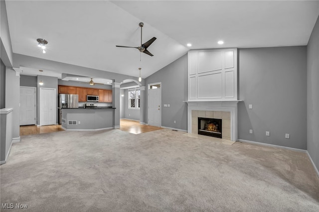 unfurnished living room featuring ceiling fan, light carpet, a tile fireplace, and vaulted ceiling