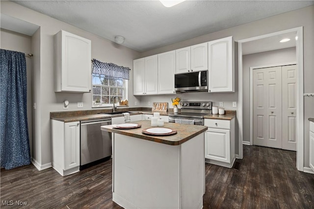 kitchen with appliances with stainless steel finishes, dark hardwood / wood-style flooring, a kitchen island, sink, and white cabinetry