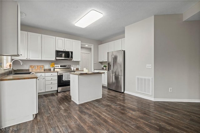 kitchen featuring stainless steel appliances, a kitchen island, dark hardwood / wood-style floors, a textured ceiling, and white cabinets