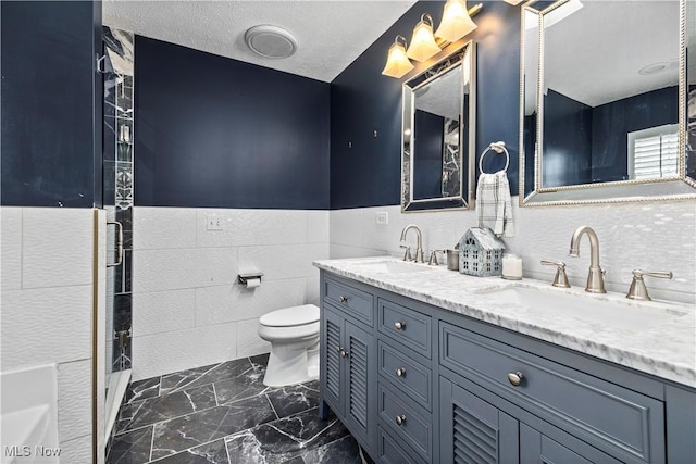 bathroom with a textured ceiling, vanity, toilet, and tile walls