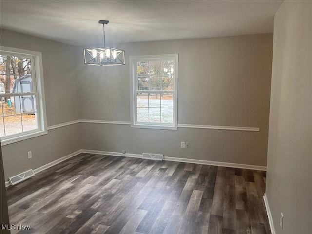 empty room with dark hardwood / wood-style flooring and an inviting chandelier