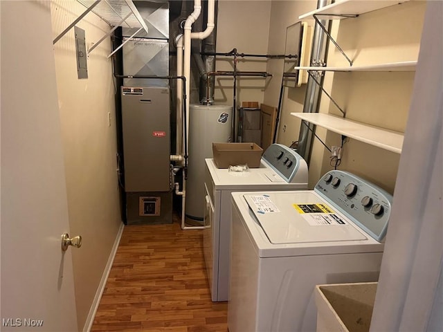 laundry area with heating unit, light hardwood / wood-style floors, water heater, and washing machine and clothes dryer