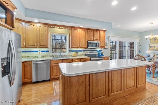 kitchen with stainless steel appliances, pendant lighting, light hardwood / wood-style flooring, a notable chandelier, and a kitchen island