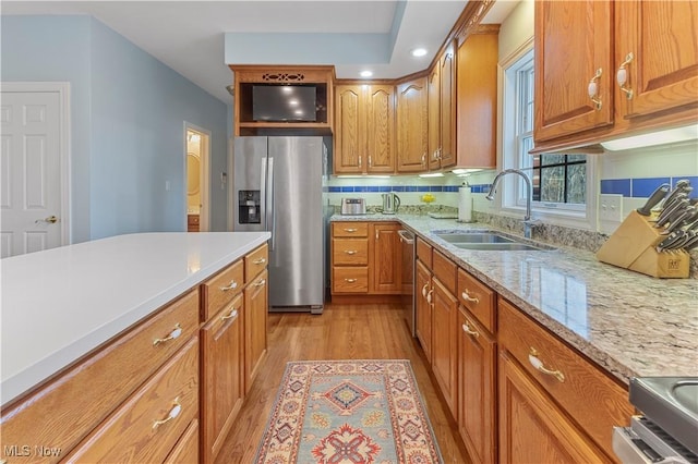 kitchen with decorative backsplash, appliances with stainless steel finishes, light wood-type flooring, light stone counters, and sink